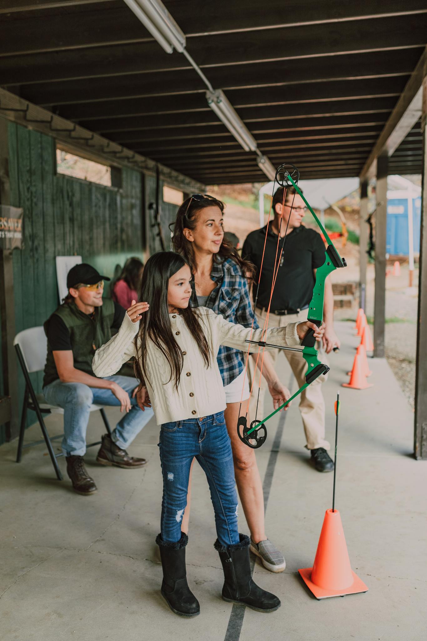 A young girl practices archery under adult supervision at an outdoor range. Engaging in target archery training.
