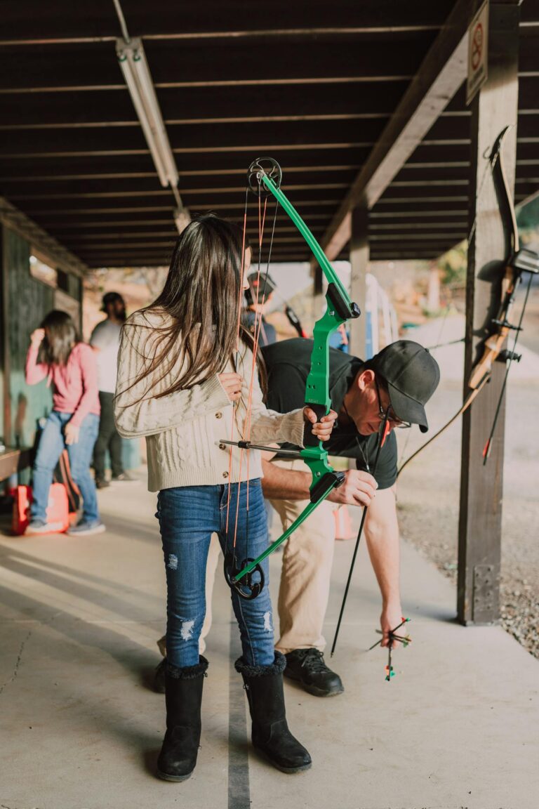 A young girl receiving archery lessons outdoors, showcasing focus and learning.