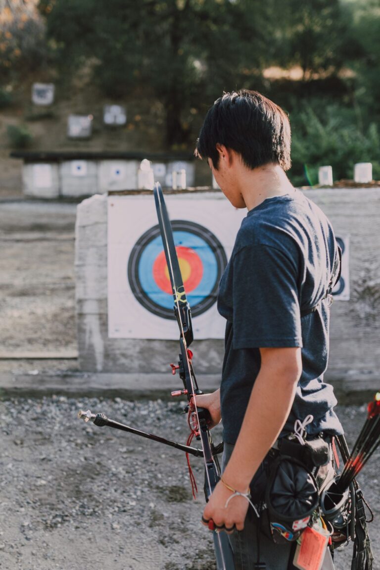 Young archer holding bow and arrow prepares to shoot at target in an outdoor range.