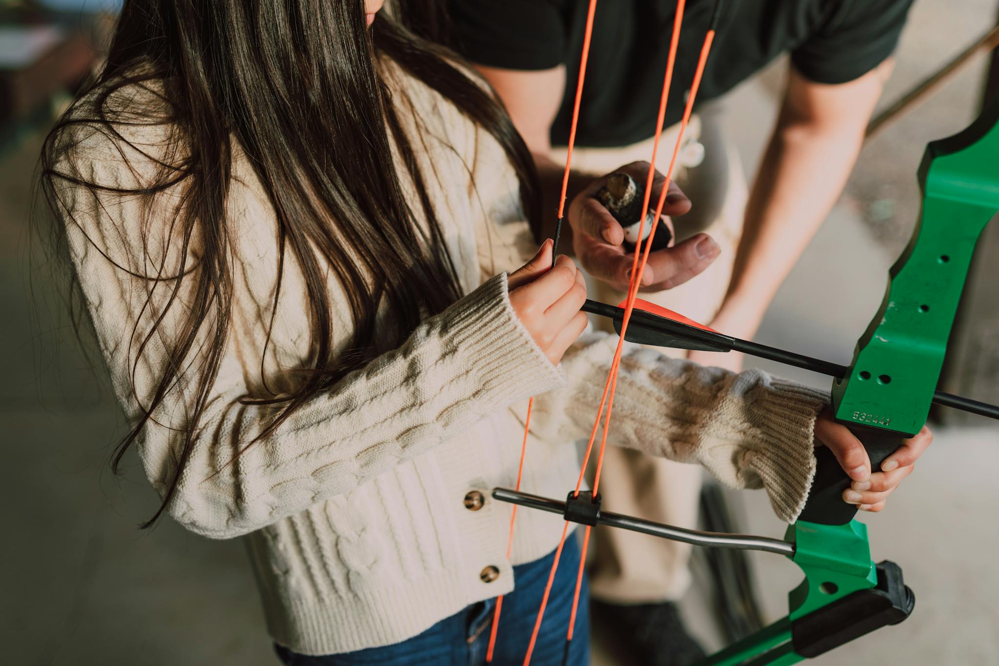 Young girl practicing archery with instructor, focusing on technique with a green recurve bow.